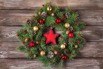 Christmas wreath made of fir tree branches, decorations, star toy, pine cones and nuts on wooden background