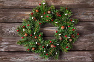 Christmas wreath made of fir tree branches, red decorations, nuts, pine cones on rustic wooden background