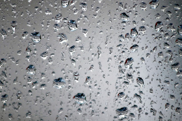 Window glas with rain drops; water drops and window wire mesh viewed from house interior