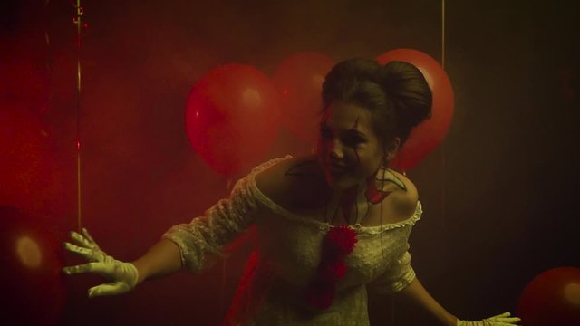 Female clown playing hide and seek. Quietly sneaking with a crazy sly predatory bloodthirsty smile. Background dark gothic room with red balls and thought fog. Face makeup paint, white vintage dress