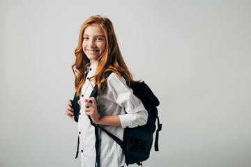 A young red-haired girl goes to school. Schoolgirl looking over her shoulder and goes to study lessons. Isolate on white background