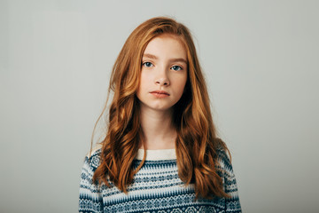 A young red-haired girl in a blue sweater looks at the camera. A girl with a worried video is trying to draw your attention to the problems of society. Isolate on a white background.