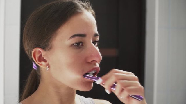 Oral hygiene for braces. Teen girl cleaning and brushing teeth with clear ceramic braces using special brushing tools. There are mirrors in the bathroom. Close-up.