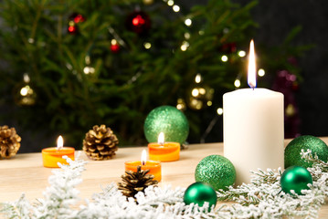 Burning candles and christmas decorations. Green balls for Christmas tree and fir twig on wooden floor with bokeh background. Copy space