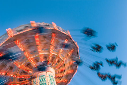 Amusement park motion blurred riders on retro vintage tilting swing against clear blue sky.