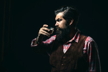 Hipster with beard and mustache in suit drinks alcohol after working day. Stylish rich man holding a glass of old whisky.