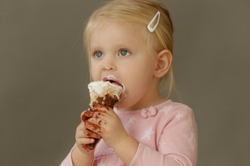 Studio shot of two years old girl eating cone ice cream. Sugar and sweets addiction concept among children. 