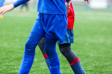 Obraz premium Boys in red and blue sportswear plays football on field, dribbles ball. Young soccer players with ball on green grass. Training, football, active lifestyle for kids concept 