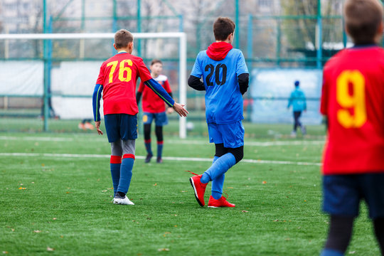 Boys in red and blue sportswear plays football on field, dribbles ball. Young soccer players with ball on green grass. Training, football, active lifestyle for kids concept 
