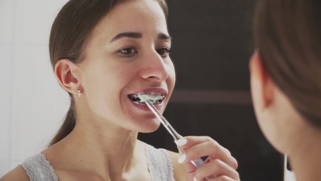 Oral hygiene for braces. A young girl in front of a mirror brushes her teeth with metal braces. Uses special toothbrushes and toothpaste. Tooth alignment. Caucasian appearance. Close-up.