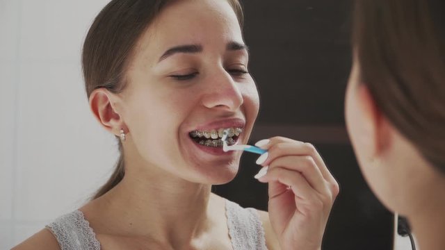 Oral hygiene with metal braces. Brushes teeth with a special toothbrush and toothpaste in the bathroom opposite the mirror. Close-up.