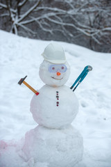 Snowman worker with hammer on snow background. Funny snowman in work helmet on snowy field....