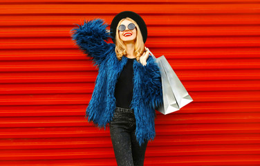 Stylish smiling woman with shopping bags enjoying new successful purchases wearing blue faux fur...