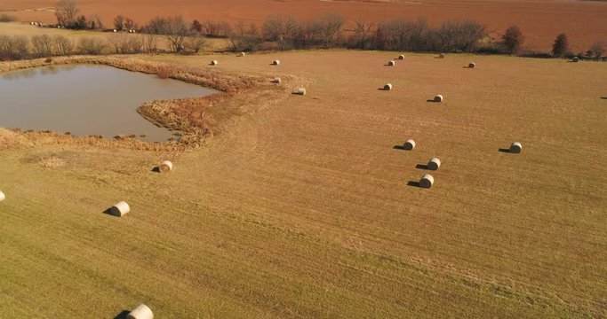 Aerial flight over large field with large round hay bales scattered