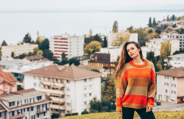 Fototapeta premium Outdoor portrait of beautiful young woman wearing warm pullover, posing on city background