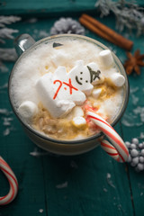 Christmas and New Year. Marshmallow snowman in hot latte in a mug. Vertical composition on a green background.