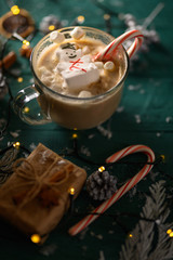 Christmas and New Year. Marshmallow snowman in hot latte in a mug. Vertical composition on a green background.