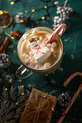 Christmas and New Year. Marshmallow snowman in hot latte in a mug. Vertical composition on a green background.
