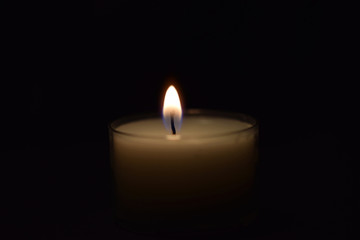 Fototapeta na wymiar Kerze leuchtet im Dunkeln - kleine weiße Kerze auf schwarzem Hintergrund