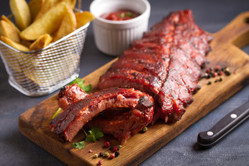 Pork loin ribs served on chopping board and potato wedges