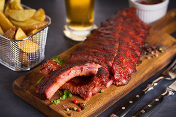 Pork loin ribs served on chopping board, potato wedges and glass of beer