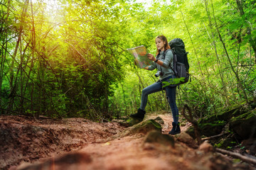Naklejka na ściany i meble woman traveler with backpack and map searching directions in the forest
