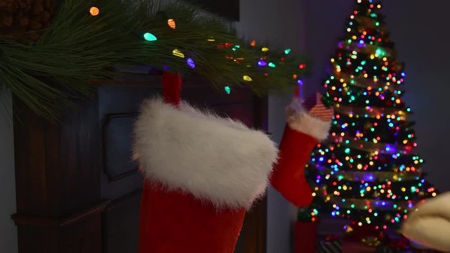 A close-up of Santa Claus&rsquo;s hand placing a large rawhide dog bone into a Christmas Stocking hanging on a mantelpiece with a Christmas tree with twinkling lights in the background.