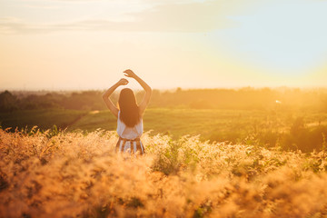 Trendy girl in stylish summer dress feeling free in the field with flowers in sunshine.