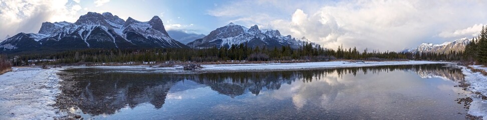 Fototapeta na wymiar Wide Panoramic Landscape of Bow River and Snowy Rocky Mountain Peaks in City of Canmore, Alberta near Banff National Park Canada