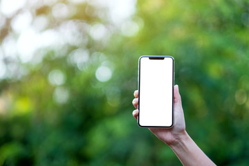 Mockup image of a hand holding black mobile phone with blank desktop screen with green nature...