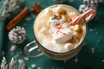 Christmas composition, mug with hot chocolate with melted snowman marshmallows and caramel. horizontal frame over green background