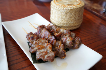 Close up Barbecue pork skewers served with a wooden basket of sticky rice ,Thai recipe