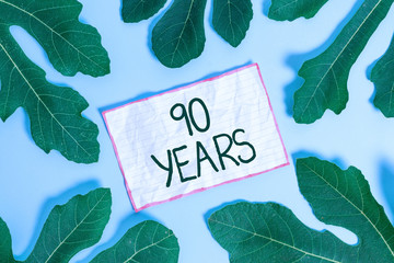 Handwriting text writing 90 Years. Conceptual photo Remembering or honoring special day for being 90 years in existence Leaves surrounding notepaper above an empty soft pastel table as background