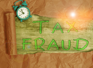 Writing note showing Tax Fraud. Business concept for entails cheating on a tax return in an attempt to avoid paying Alarm clock and torn cardboard on a wooden classic table backdrop
