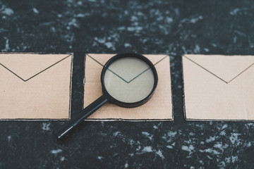 filtering your inbox against spam, magnifying glass analyzing a specific email envelope out of a group