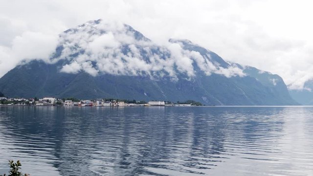 View to the beautiful Norwegian village with the traditional red and white houses at the fjord. Mountains covered with clouds on a rainy day.