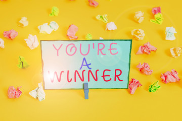 Text sign showing You Re A Winner. Business photo showcasing Winning as 1st place or the champion in a competition Colored crumpled papers empty reminder white floor background clothespin