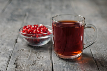 Glass mug with pomegranate juice and pomegranate seeds on a black wooden table.
