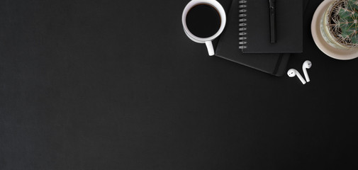 Top view of dark trendy workplace with coffee cup and office supplies on black table
