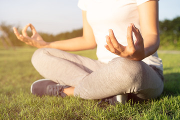 Hand of woman in lotus pose sitting on green grass and blurred background in the park, Concept of relaxation and meditation.