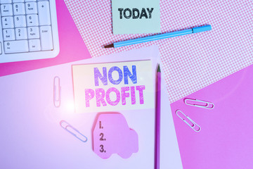 Writing note showing Non Profit. Business concept for type of organization that does not earn profits for its owners Writing equipments and computer stuffs placed above colored plain table