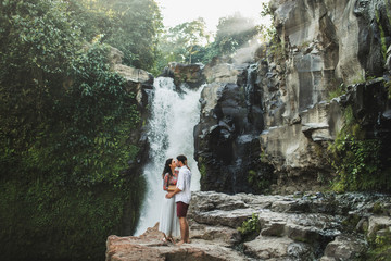 Young couple in love kissing with amazing view of Tegenungan cascade waterfall. Happy together,...
