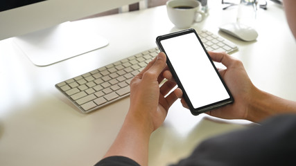 Cropped shot young man holding empty screen of mobile phone on office desk.