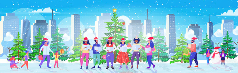 people with sheet books giving performance merry christmas happy new year holidays celebration concept mix race men women standing near fir tree modern cityscape background full length horizontal