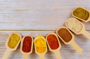 Assortment of colorful spices in the wooden spoons on wooden background.