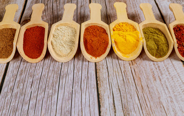 Colored ground spices powders in wooden spoons on white wooden background.