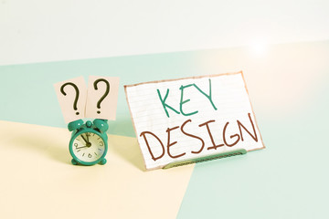 Handwriting text Key Design. Conceptual photo a necessary or very important realization of a concept or idea Mini size alarm clock beside a Paper sheet placed tilted on pastel backdrop