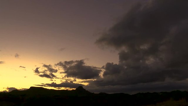 Peaceful and beautiful sunset timelapse over desert mountains with purple, orange, and yellow clean skies behind dark storm clouds