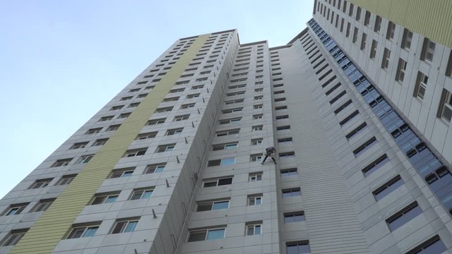 A building maintenance worker repairing paintwork is abseiling and traversing from the top of a massive high rise building facade in Seoul South Korea. Low, wide angle