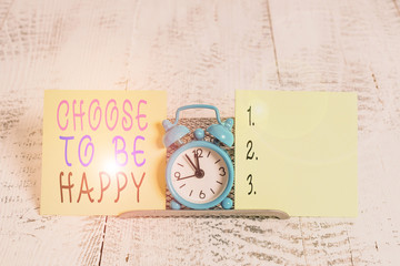 Writing note showing Choose To Be Happy. Business concept for Decide being in a good mood smiley cheerful glad enjoy Mini blue alarm clock standing above buffer wire between two paper